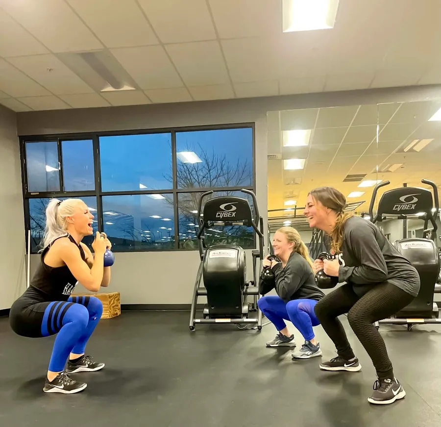 Three members doing kettlebell squats together and laughing