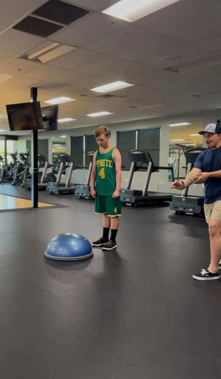 A coach guiding an athlete through balance training on a Bosu ball