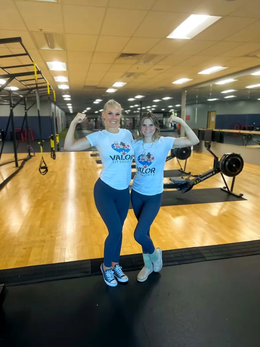 Johnna and her daughter Jade flexing in Valor Fit Society shirts at the gym