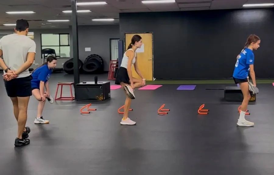 A group of teen athletes doing agility hurdle drills with a coach