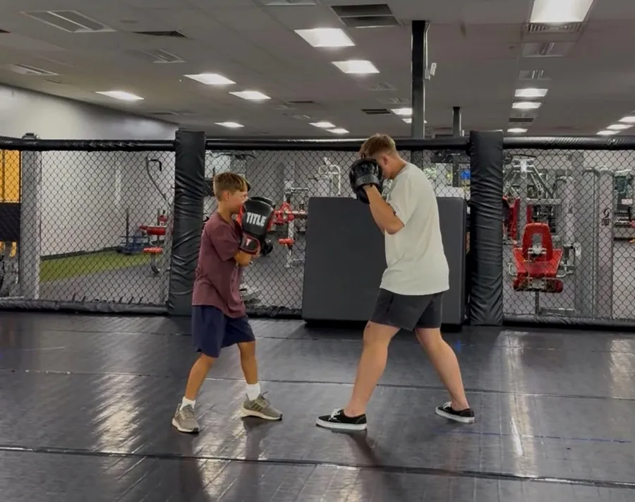 Two young athletes sparring with pads in the training cage at Valor Fit Society