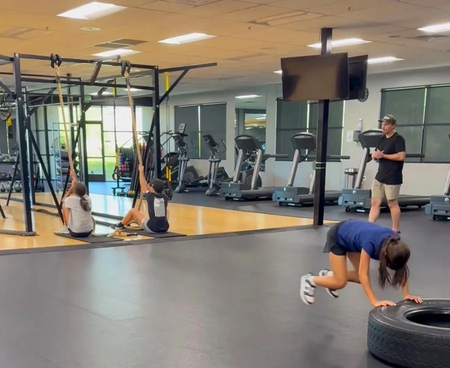 A young athlete flipping a tire while others train on ropes in the background
